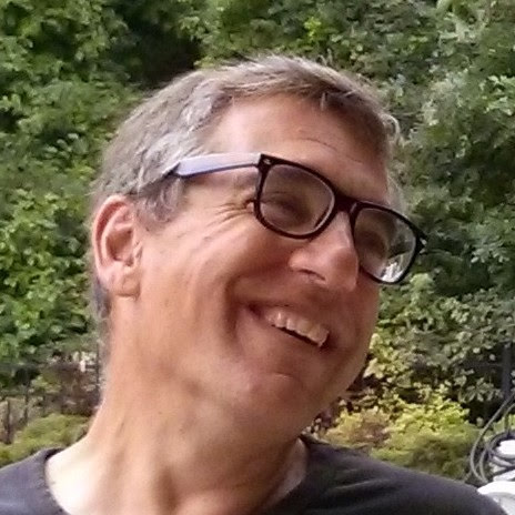 Author Robert Schechter - headshot with him looking upward to the right and smiling. They are wearing black framed glasses.