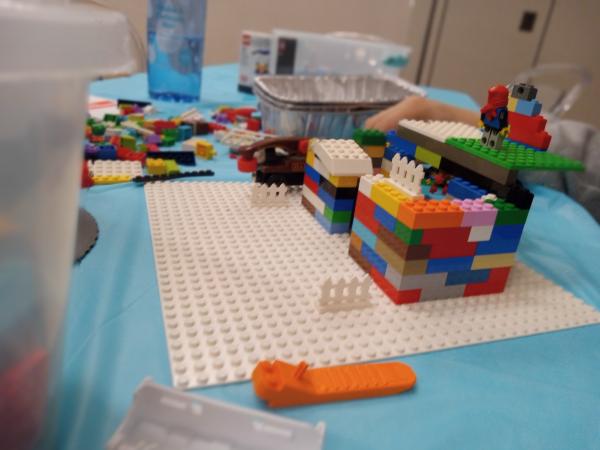 Photo features a colorful building made of legos on a white lego mat. Various lego pieces surround the matt waiting to incorporated into the unfinished build.